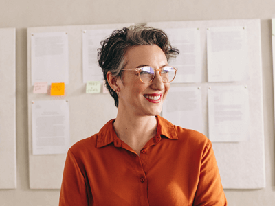 Middle aged woman wearing glasses standing in front of a wall of notes in an office